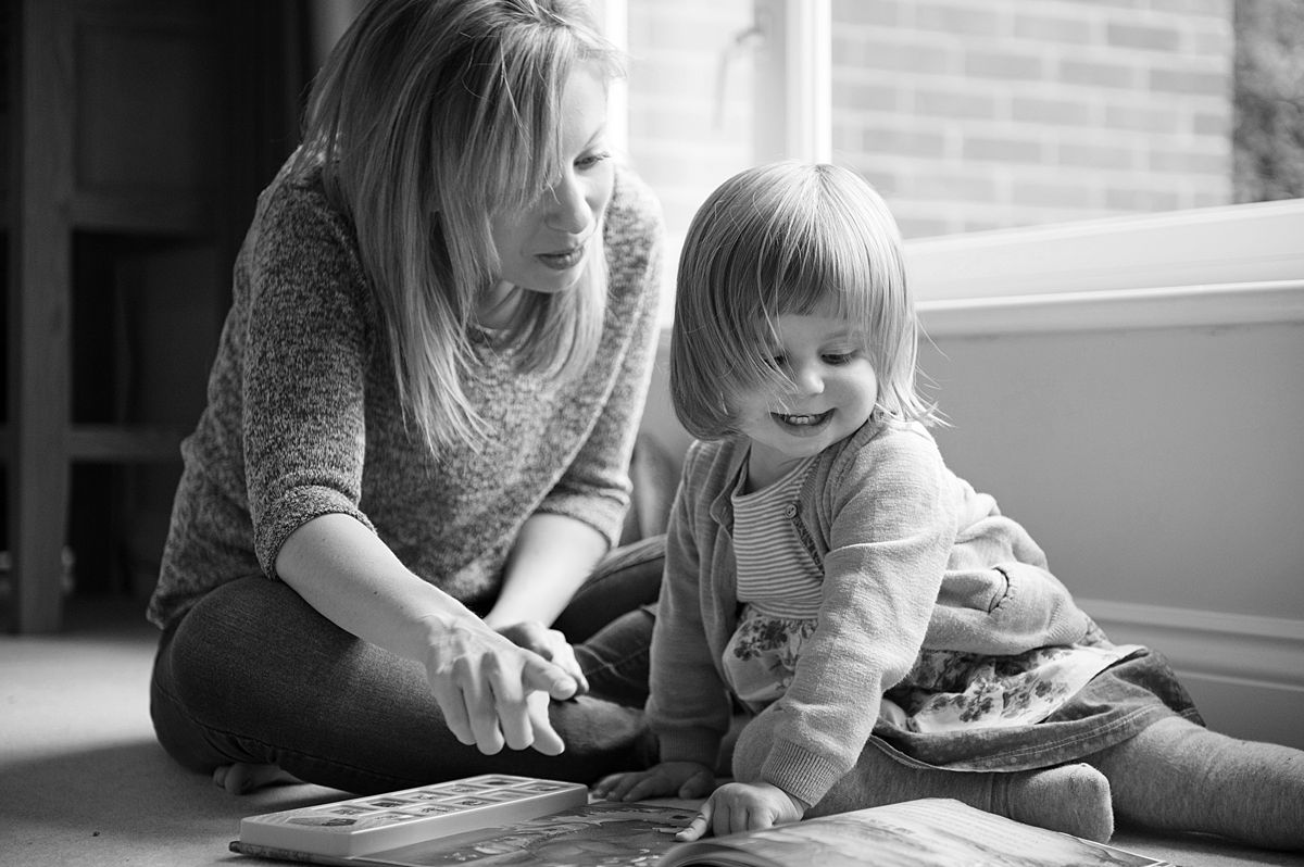 Family-Photography-Basingstoke-Winchester_0244 mother and toddler daughter reading a book together while sitting on the carpet during a family photography session.