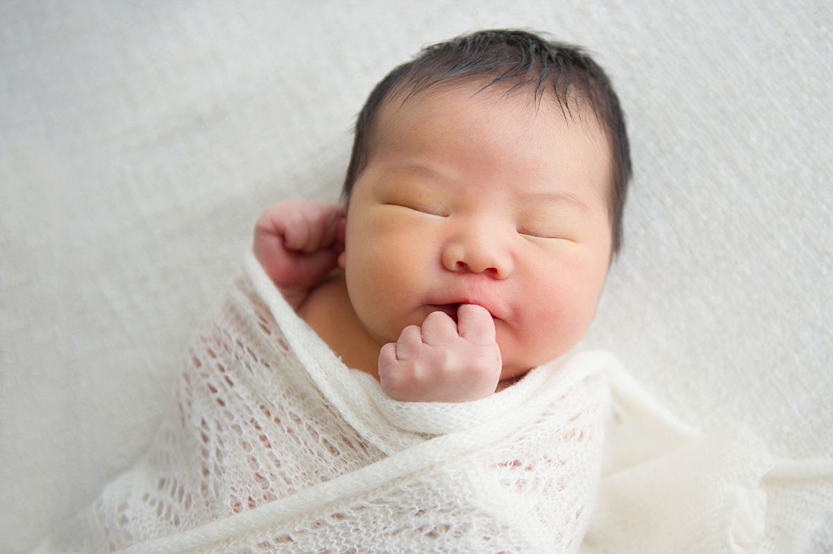 Newborn-Photography-Reading newborn baby swaddled in knit wrap and sleeping with hand by his face - newborn photography reading