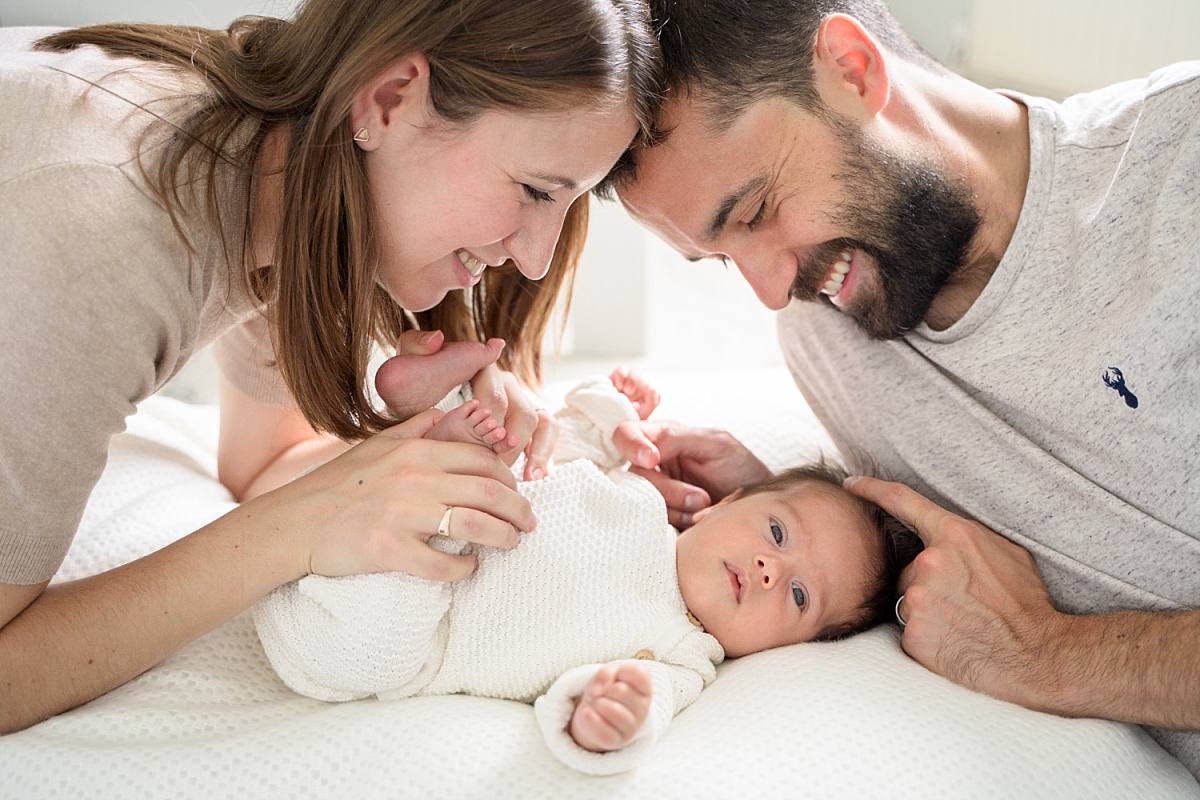family photography with a baby in reading mum and dad looking over wide awake newborn and smiling. Baby wearing a white knit outfit - newborn photography reading