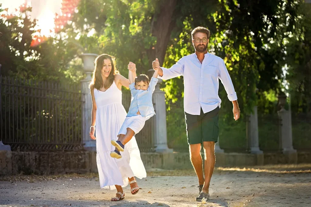Family walking through a local park swinging their little boy in the air during an outdoor family photoshoot in Palermo, Sicily by family photographer Maria Cristina Licata.