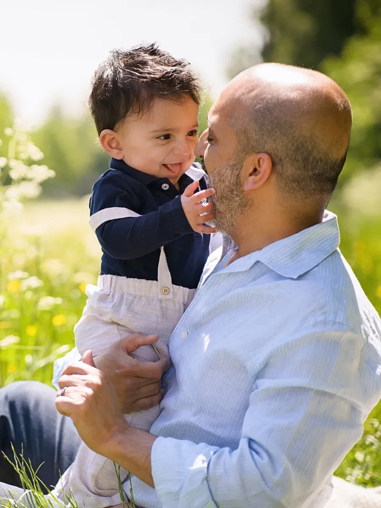 Smiling toddler holds daddy's face in a playful outdoor family portrait captured by Hampshire family photographer Maria Cristina Licata