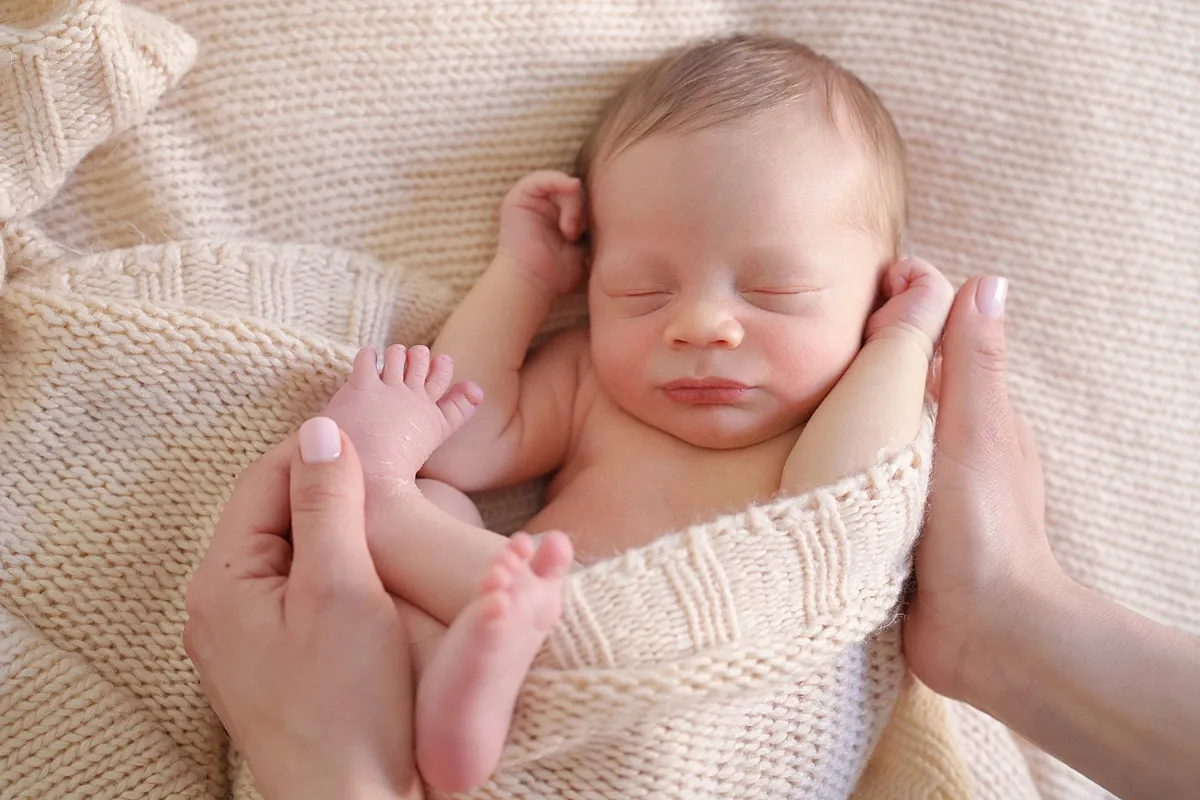 newborn_photoshoot_at_home_0034_webp newborn baby swaddled in a cosy blanket and held by mum's hands on a neutral background - newborn photography in reading