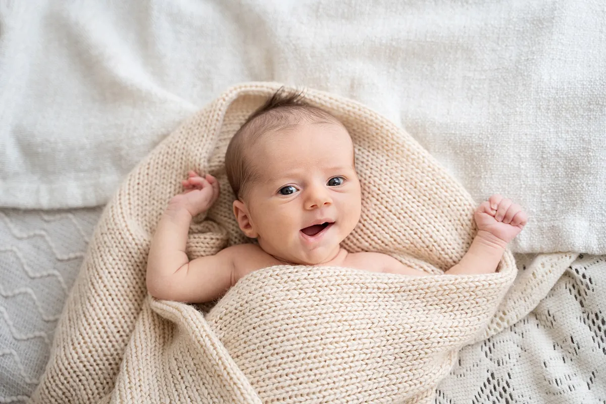 studio_newborn_photoshoot_0014_webp a wide awake newborn baby smiling while wrapped in a beige blanket during a newborn photoshoot in Basingstoke
