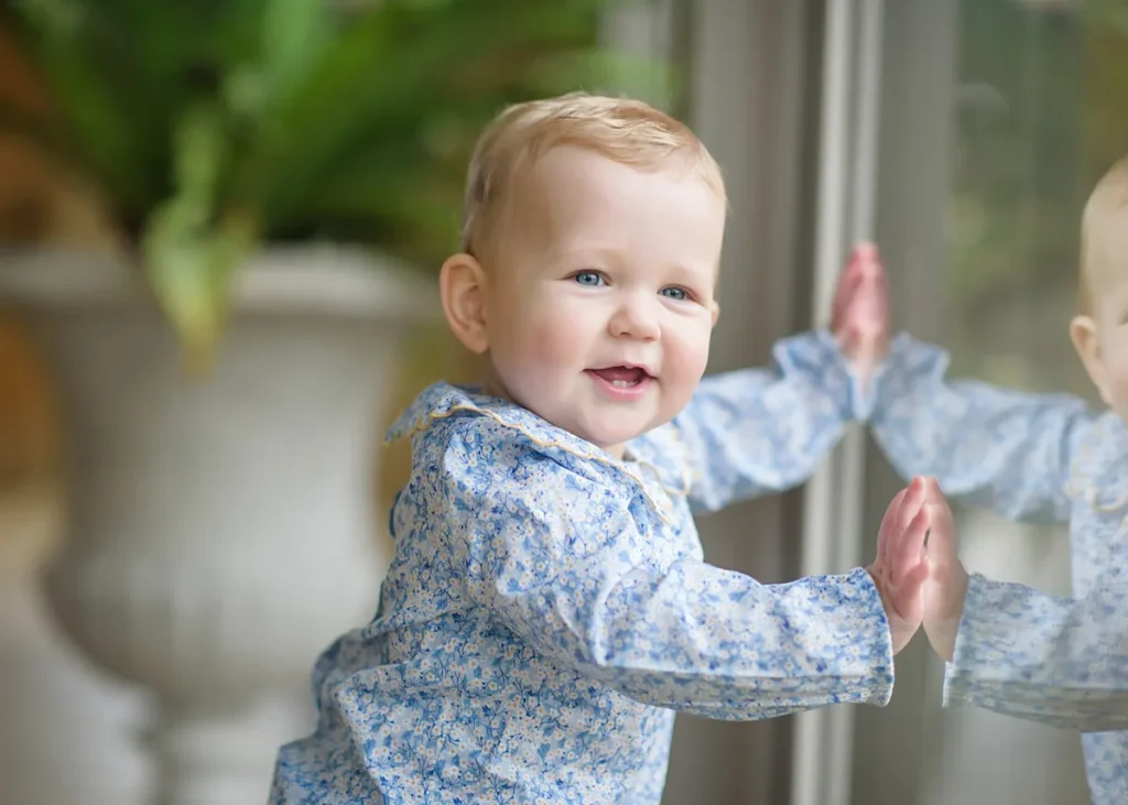 smiling toddler girl leaning on window in a classic baby portrait at home in the Cotswolds. captured by Berkshire family photographer Maria Cristina Licata