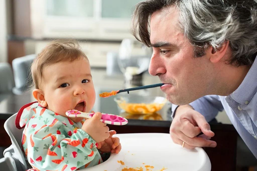 Baby being playfully fed by dad during a lifestyle family photo session at home in London. Captured naturally by London family photographer Maria Cristina Licata