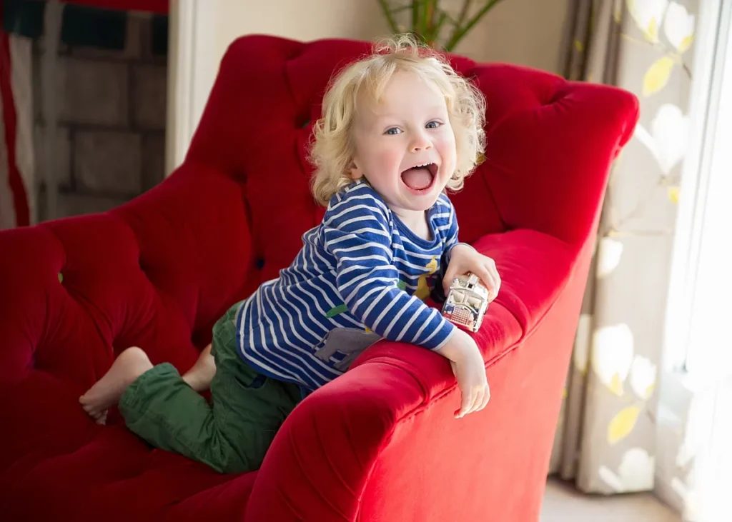 Toddler playing with toy car on the sofa during a natural photoshoot at home. captured naturally by Hampshire family photographer Maria Cristina Licata.