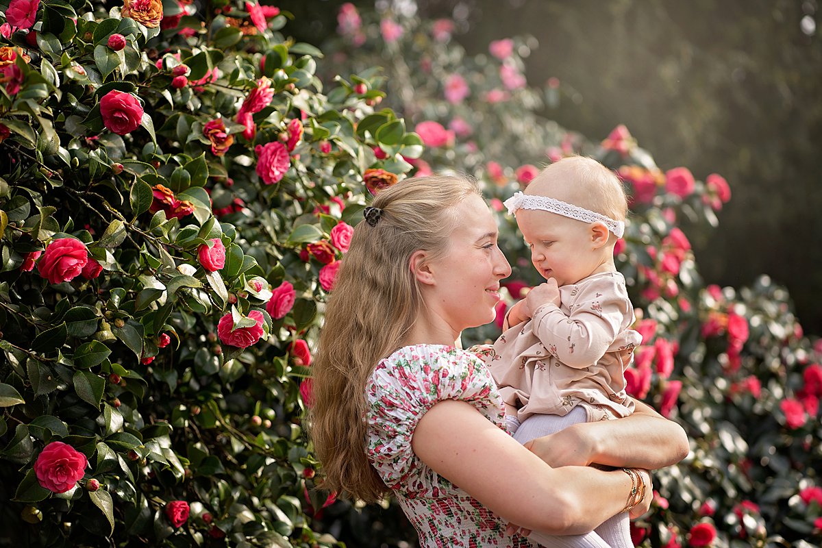 natural portrait of a mum holding baby girl in front of a camellia bush, taken by a family photographer