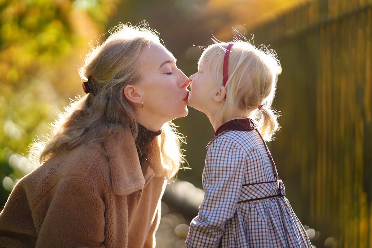 autumn-family-photoshoot_0081 Tender mother-daughter moment sharing a gentle kiss in golden sunlight, showcasing the beautiful bond during an autumnal outdoor family portrait session in Hampstead heath by Maria Cristina Licata.