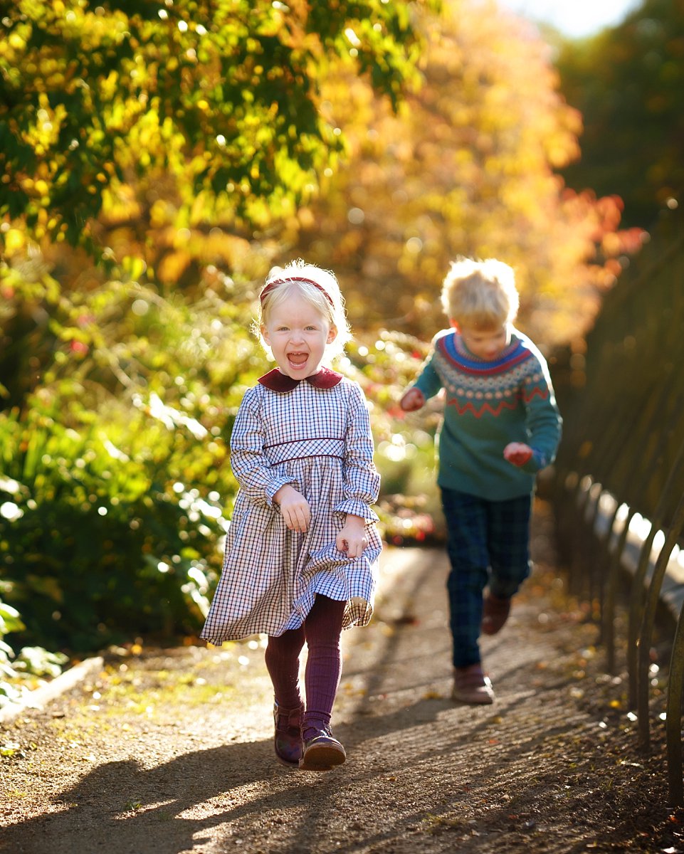 autumn-family-photoshoot_0124 Two young siblings in stylish winter fashions playing chase during an autumn family photoshoot at Hampstead Heath – candid seasonal photography by The Childhood Photographer.