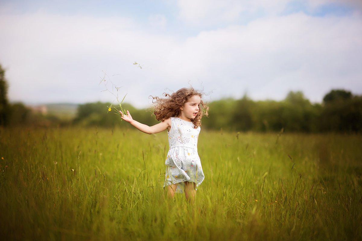 summer-family-photoshoot_0085 Joyful child running through a meadow with arms outstretched, capturing carefree childhood moments in natural light – outdoor family photography in Surrey by Maria Cristina Licata.