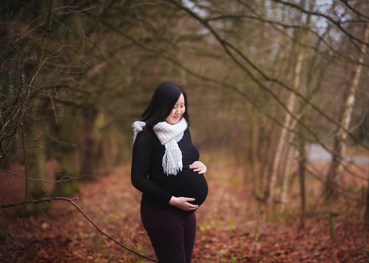 winter-family-portraits_0069 Serene expectant mother cradling her bump in a peaceful woodland setting, documenting the beautiful anticipation of new life in a maternity photoshoot by Maria Cristina Licata.