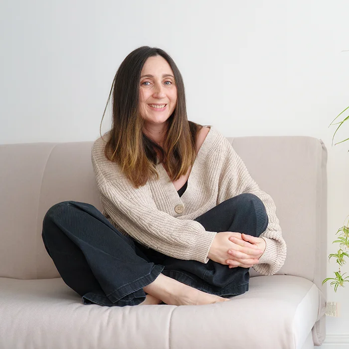 a portrait of family photographer Maria Cristina Licata, sitting on a sofa cross-legged and smiling