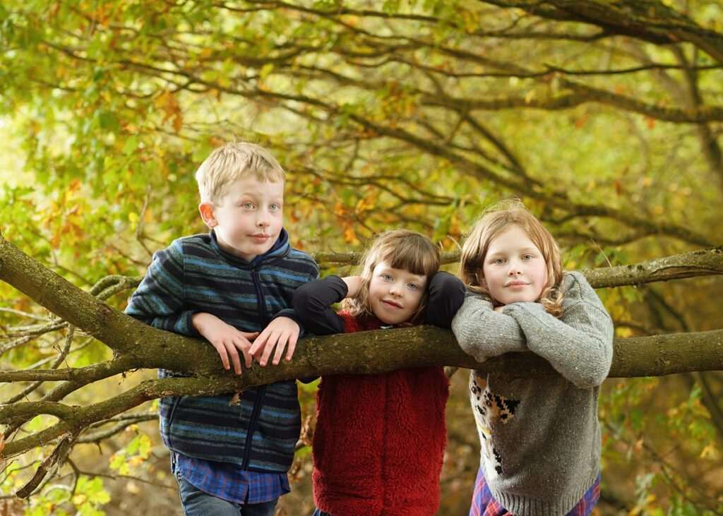 natural family portrait of smiling siblings by a large tree, taken on a family photoshoot at Dinton Pastures, Reading.