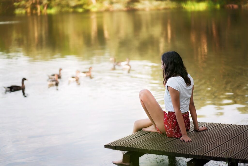 natural portrait of a girl sitting on a jetty, looking at passing ducks, taken on a photoshoot at Dinton Pastures, by a Reading family photographer.
