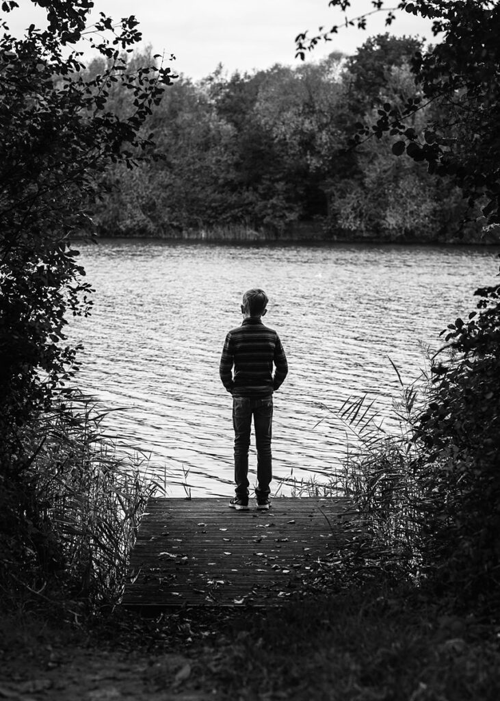 dramatic black and white portrait of a boy on a jetty, looking out towards a lake. Taken at Dinton pastures, in Reading, by a Reading family photographer