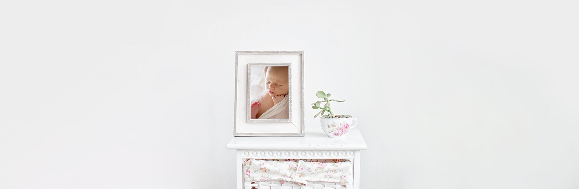 a portrait of a newborn baby set in a white distressed wooden frame, sitting on top of a small cabinet.