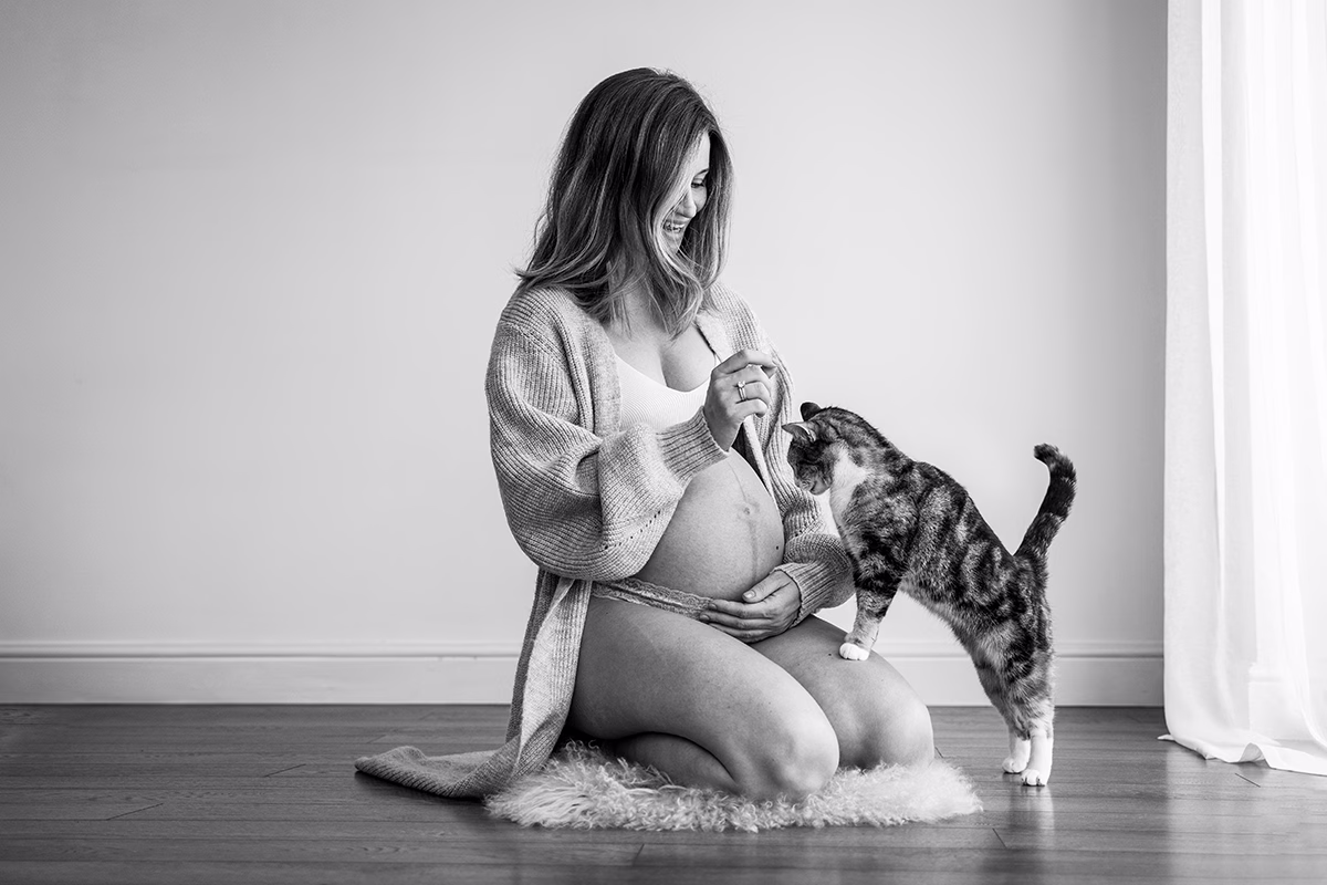 A pregnant woman plays with a cat. A playful moment from a studio maternity photo shoot with Hampshire family photographer Maria Cristina Licata